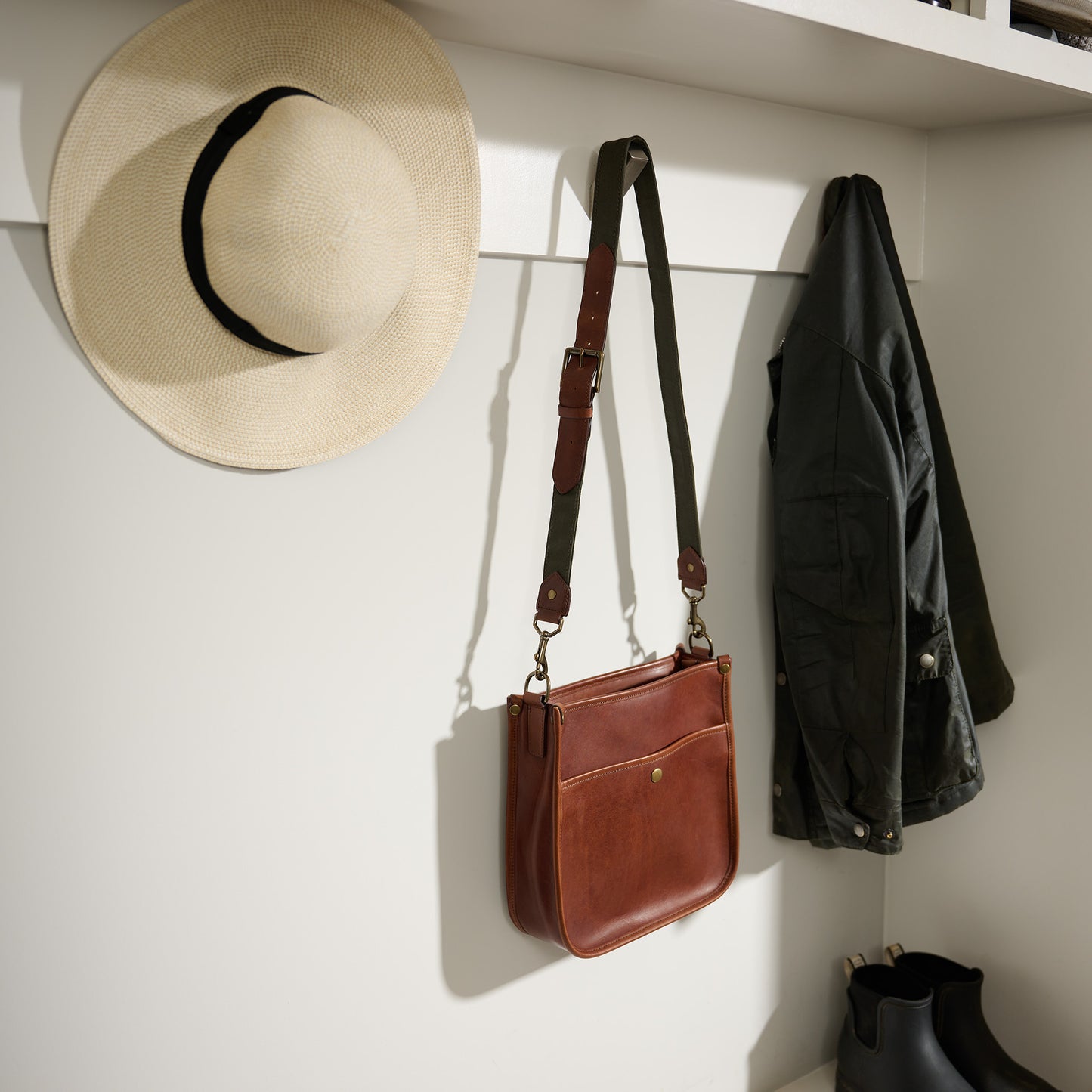 Cumberland Crossbody in vintage brown full grain leather and green strap hanging on coat rack