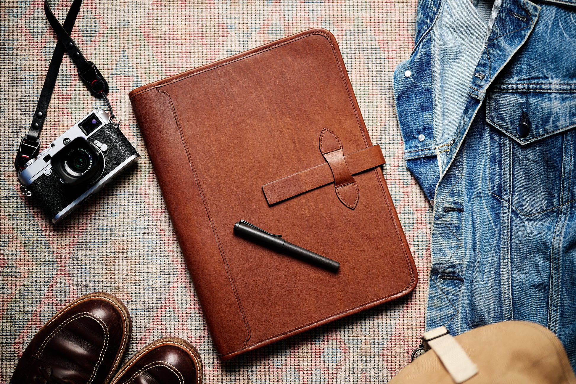 full grain leather portfolio closed in vintage brown color flat lay with denim and camera in background