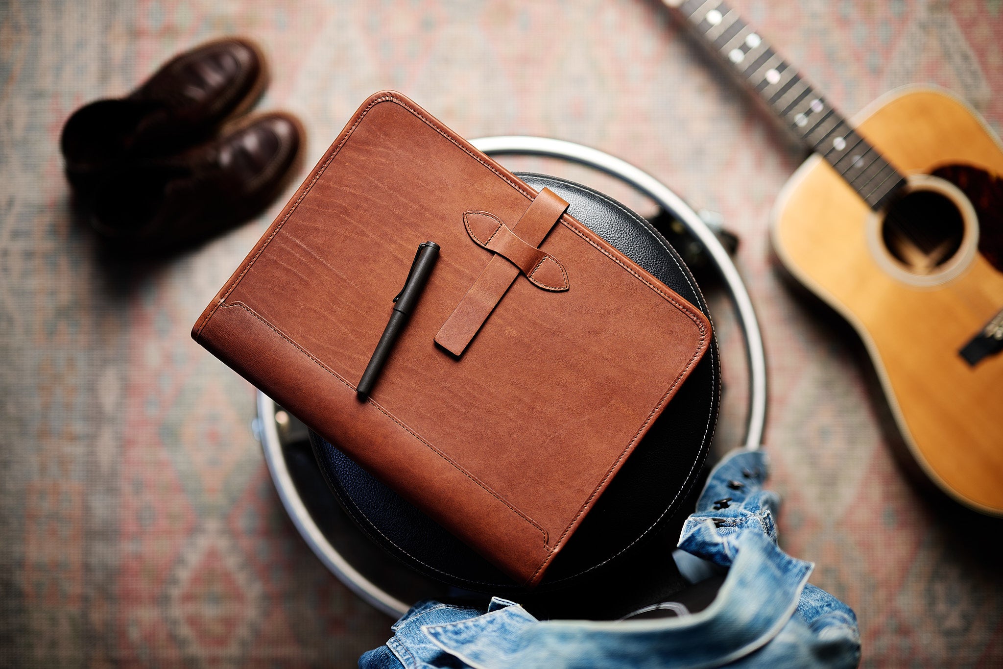 full grain leather portfolio flat lay with guitar in background - vintage brown color