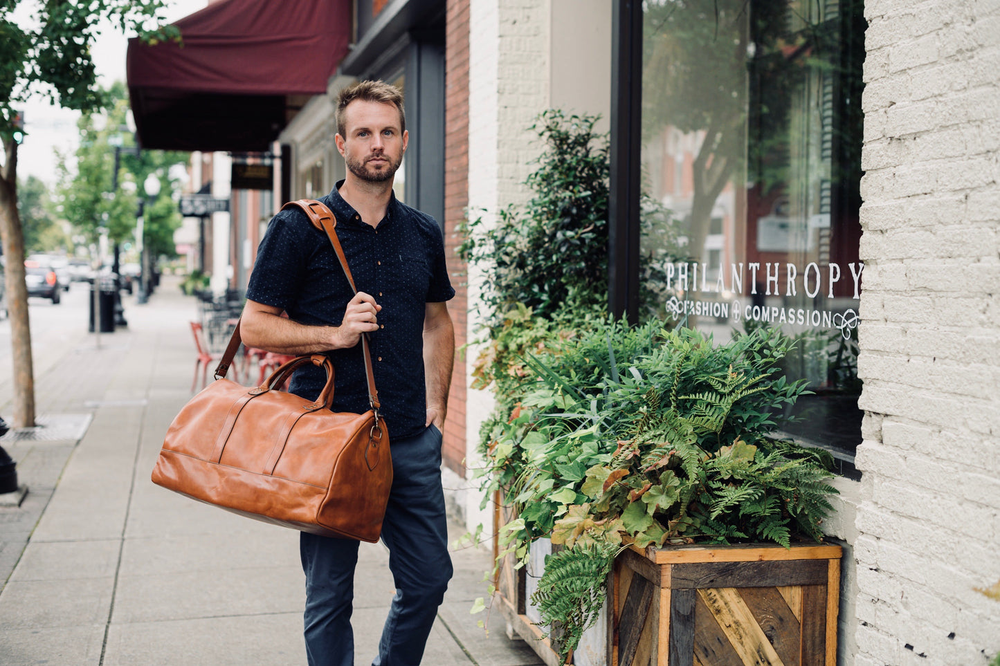 Jackson Wayne Big Sur Duffle Bag lifestyle shot in saddle tan walking on street with shoulder strap - full grain leather